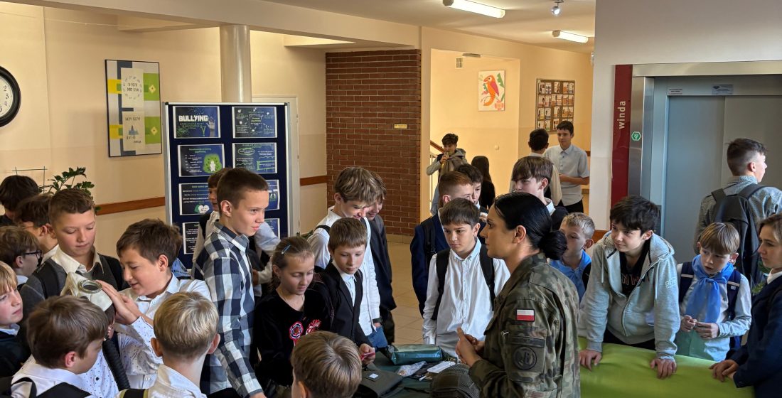 zdjęcie przedstawia żołnierza WP w otoczeniu uczniów przy stoisku ze sprzętem wojskowym