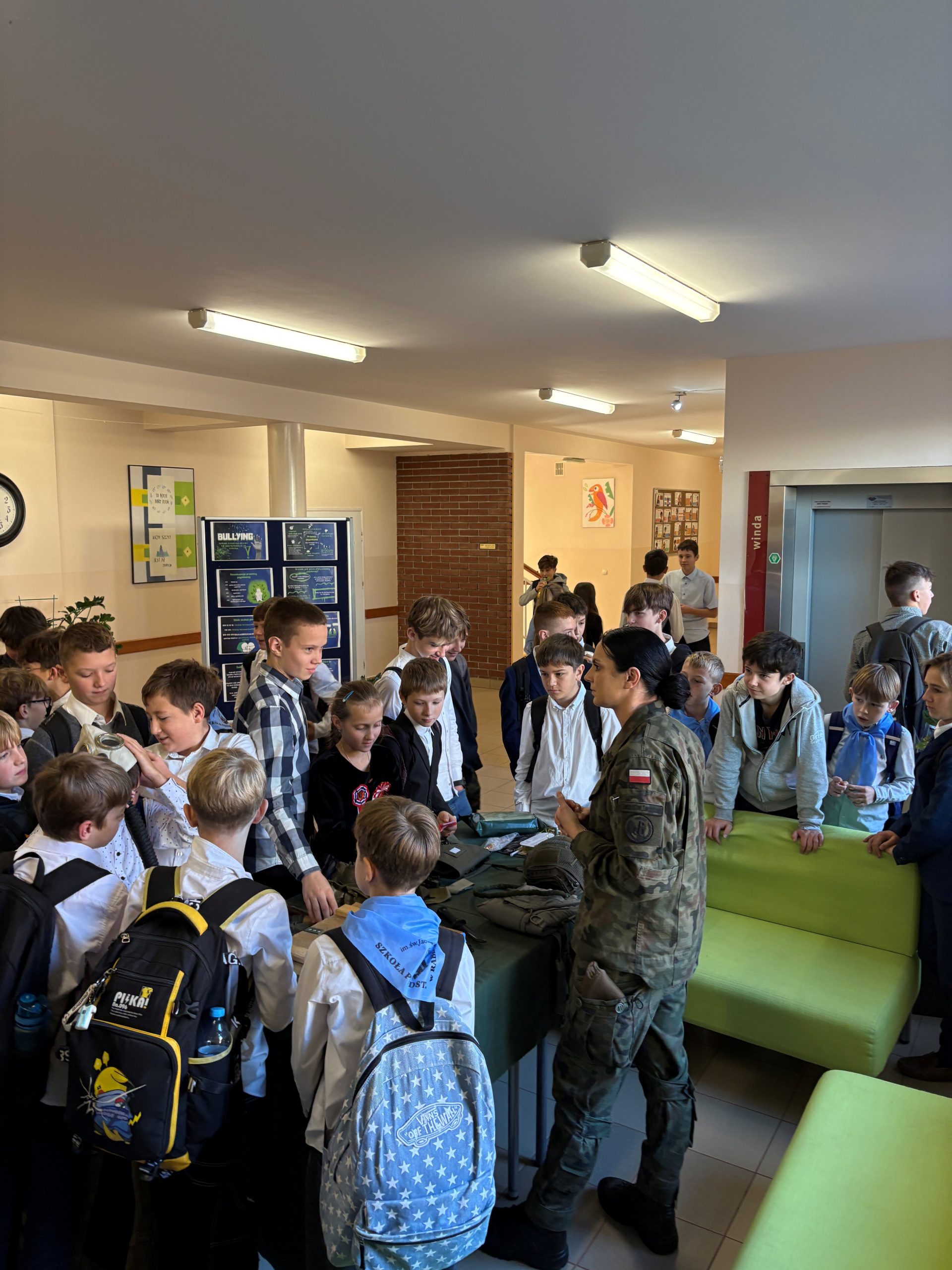 zdjęcie przedstawia żołnierza WP w otoczeniu uczniów przy stoisku ze sprzętem wojskowym